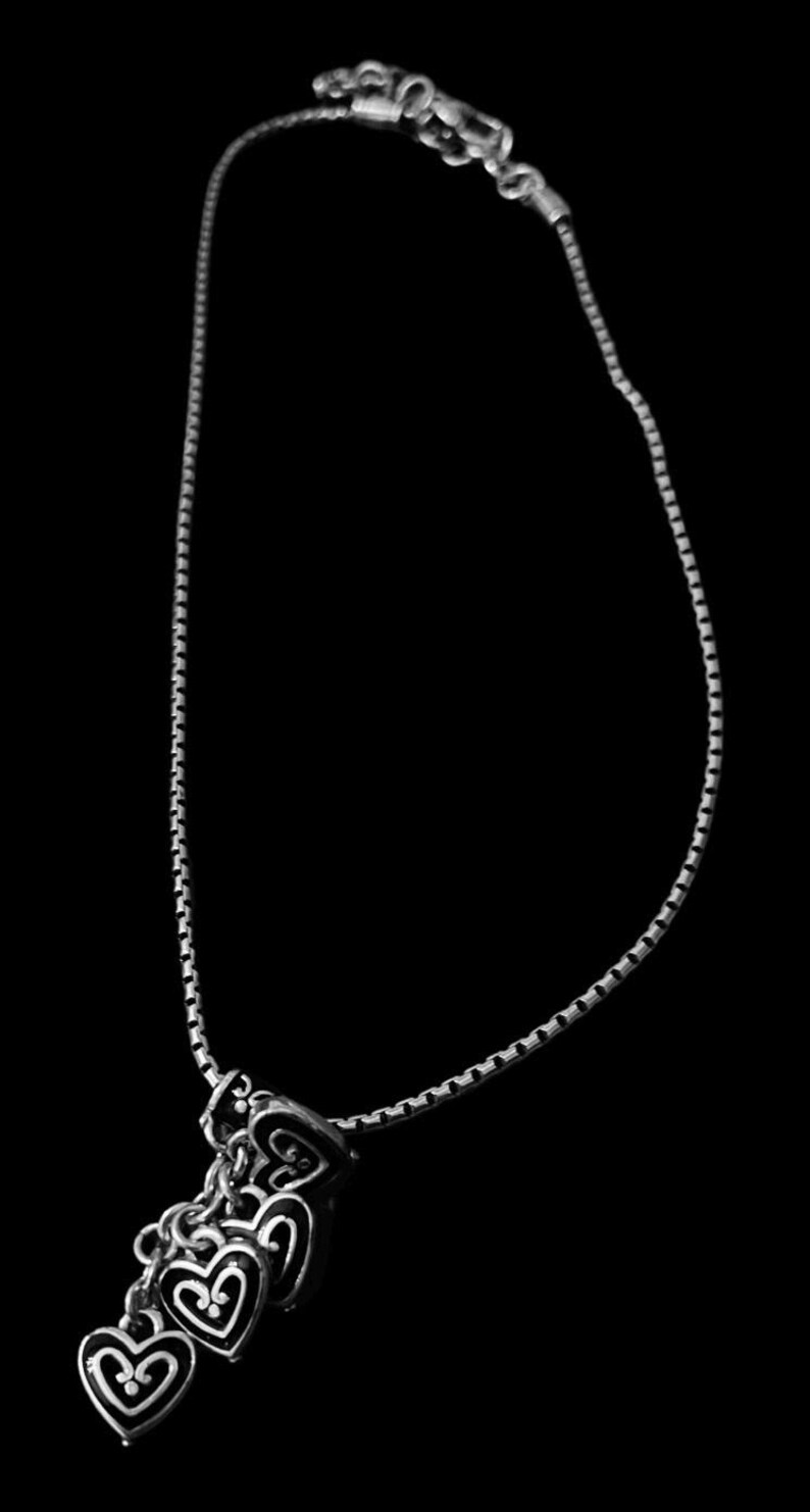 Może przedstawiać: Srebrny naszyjnik z łańcuszkiem i zawieszką w kształcie kilku srebrnych serc. Każde serce ma szczeg&oacute;łowy wz&oacute;r.