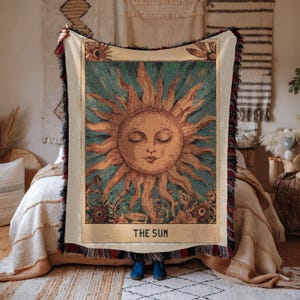 Boho woven blanket showing a tarot card in vintage style, representing "The Sun" card. Cosy throw blanket in 100% cotton, with a sunny and spiritual design in warm and natural colors. Perfect for cozy evenings at home or outdoor, available in three sizes. Must have for anyone who wants to add warm and positive decor to its home. Great gift for yourself or others.