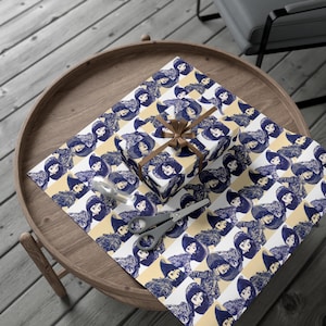 Könnte beinhalten: Ein verpacktes Geschenk und Geschenkpapier mit einem sich wiederholenden Muster eines Frauenporträts in Marineblau auf einem weiß-gelb gestreiften Hintergrund. Ein braunes Band ist um die Schachtel gebunden. Schere und Klebeband sind ebenfalls sichtbar.