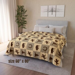 Könnte beinhalten: Eine beige-graue karierte Decke mit braunen Cowboy-Motiven, darunter Hufeisen, Bullen und Pferde. Die Decke wird auf einem Bett präsentiert und misst 152 cm x 203 cm.