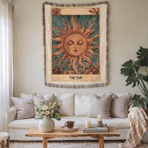 Boho woven blanket showing a tarot card in vintage style, representing "The Sun" card. Cosy throw blanket in 100% cotton, with a sunny and spiritual design in warm and natural colors. Perfect for cozy evenings at home or outdoor, available in three sizes. Must have for anyone who wants to add warm and positive decor to its home. Great gift for yourself or others.