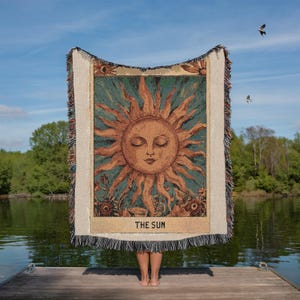 Boho woven blanket showing a tarot card in vintage style, representing "The Sun" card. Cosy throw blanket in 100% cotton, with a sunny and spiritual design in warm and natural colors. Perfect for cozy evenings at home or outdoor, available in three sizes. Must have for anyone who wants to add warm and positive decor to its home. Great gift for yourself or others.