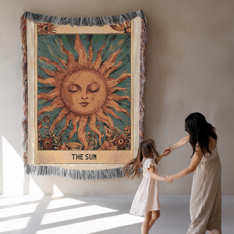 Boho woven blanket showing a tarot card in vintage style, representing "The Sun" card. Cosy throw blanket in 100% cotton, with a sunny and spiritual design in warm and natural colors. Perfect for cozy evenings at home or outdoor, available in three sizes. Must have for anyone who wants to add warm and positive decor to its home. Great gift for yourself or others.