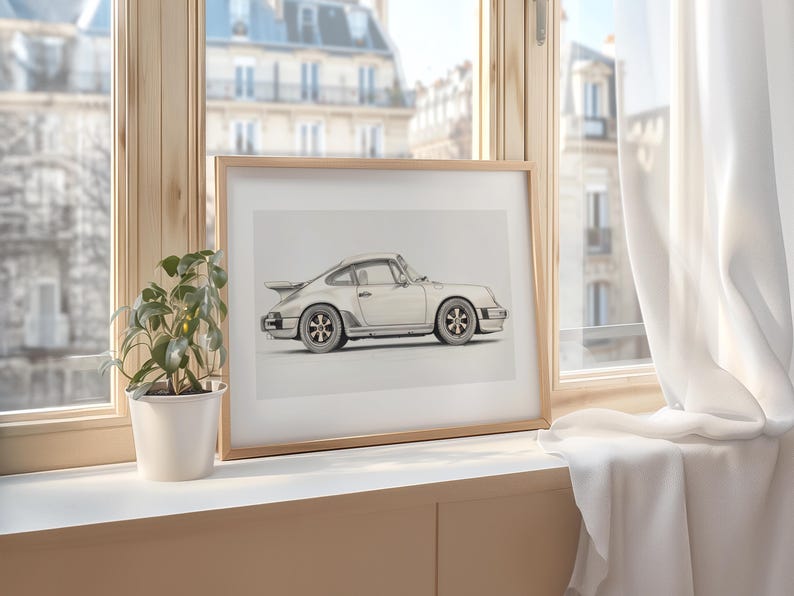May include: A framed print of a white Porsche 911 car on a light wood windowsill. The car is drawn in a realistic style with a light gray background.