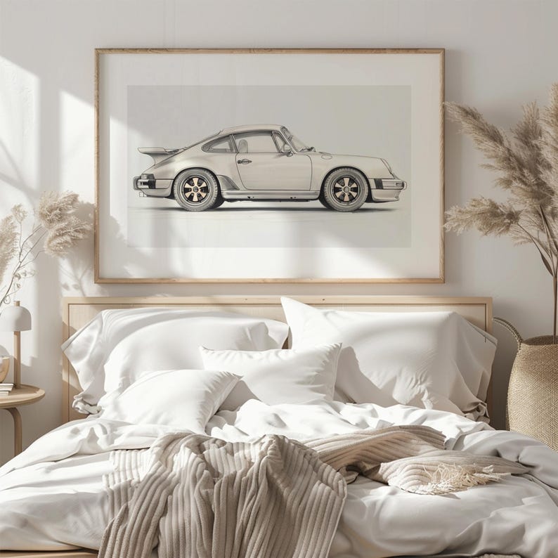 May include: A white Porsche 911 car print in a wooden frame hanging above a white bed with a beige blanket and pillows.