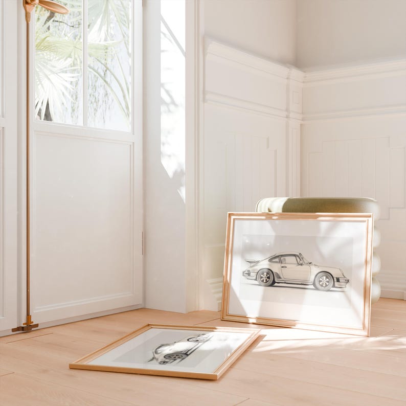 May include: Two framed prints of a vintage car in a light beige color. The prints are in gold frames and are on a light wood floor.