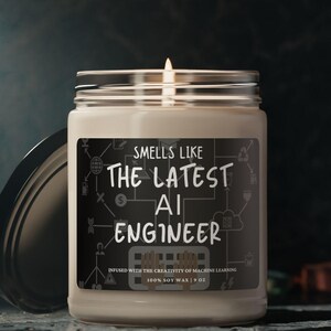 May include: A white candle with a black label that reads "Smells Like The Latest AI Engineer" with a graphic of a circuit board and code. The candle is in a glass jar with a black lid.