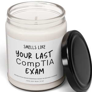 May include: A white candle in a clear glass jar with a black lid. The label reads "Smells Like Your Last CompTIA Exam" and "Infused with the bittersweet scent of second-guessing. 100% Soy Wax | 9 oz."