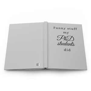 May include: Open, light grey journal with the text "Funny stuff my PhD students did" in black. The journal is open, revealing blank pages. The cover has a barcode sticker.