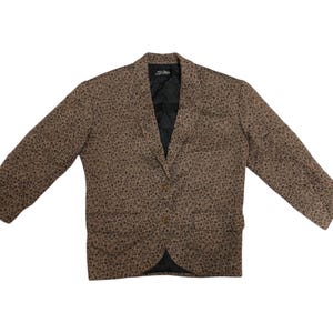 May include: Brown blazer with a small, dark pattern. The blazer has a notched lapel, two front pockets, and a two-button closure. The sleeves are long, and the blazer is fully lined with a black fabric. The blazer is laid flat on a white background.