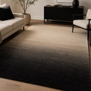 May include: A rectangular area rug with a gradient design, transitioning from black at the bottom to beige at the top. The rug is placed on a hardwood floor, and the room features a sofa, chair, and decorative items.