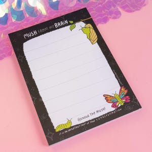 May include: Black notepad with white lined paper and a black border. The notepad has a white and green caterpillar, a green and yellow butterfly, and the text "Mush from my brain" and "Honour the mush! It is an important part of your transformation".