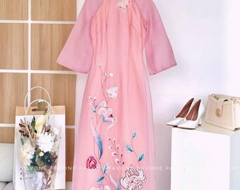 May include: A pink long-sleeved dress with a high neckline and floral embroidery. The dress has a sheer overlay and is hanging on a white hanger.