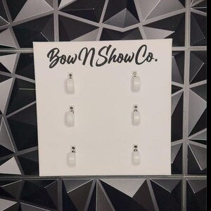 May include: White display board with the text "Bow N Show Co." printed in black. The board has six white plastic hooks.