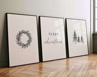 May include: Three framed Christmas art prints. The prints feature a wreath, the words "Merry Christmas", and a winter forest scene. The frames are black, and the background is a neutral color.