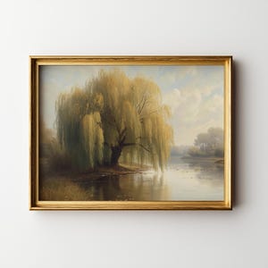 May include: A framed landscape painting depicts a large weeping willow tree on the edge of a calm river. The tree's yellow-green leaves cascade down, and the water reflects the sky and distant trees. The frame is gold.