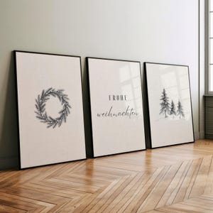 May include: Three framed art prints with black frames. The prints feature a wreath, the text "FROHE weihnachten", and a forest scene. The art has a neutral color palette, with black and white illustrations on a beige background.
