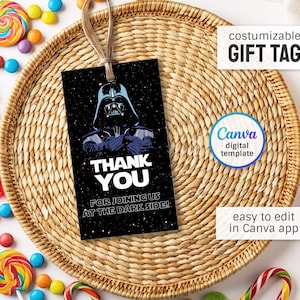Peut inclure: Une étiquette cadeau noire avec Dark Vador et le texte "THANK YOU FOR JOINING US AT THE DARK SIDE!". L'étiquette est personnalisable et facile à modifier dans l'application Canva. L'étiquette est attachée à un panier tressé avec un ruban.