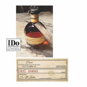 May include: A custom wedding label for Blanton's Gold Bourbon Whiskey. The label is printed on a cream-colored paper with a brown border. The text on the label reads "Chuck, We would be honored if you did the honors. WILL YOU MARRY US? SAT 10142025 Requested by Tim & Dahlia 46.54 ALC/VOL (93 PROOF) Blanton's Gold Bourbon Whiskey ITHACA NEW YORK".