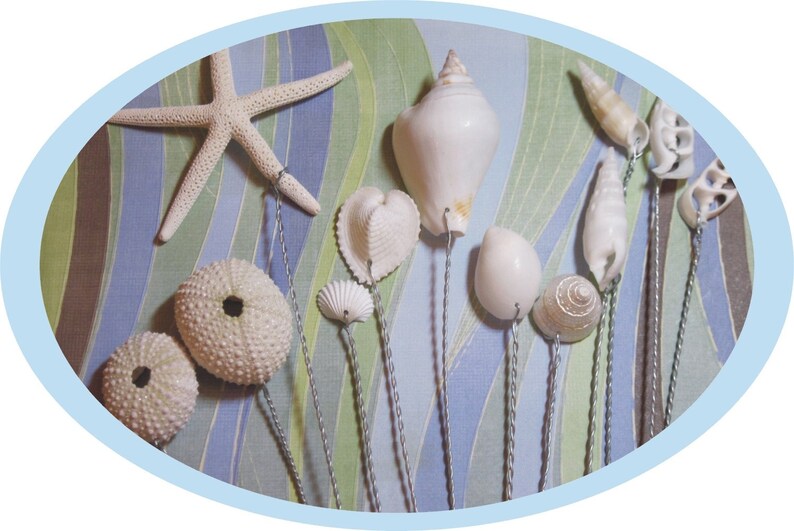 May include: A collection of white seashells and starfish on wire stems, arranged on a blue and green striped background.