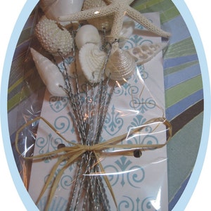 May include: A bouquet of white seashells and a white starfish tied with a brown ribbon. The bouquet is wrapped in clear plastic and is sitting on a white and blue patterned surface.