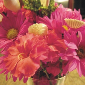 May include: A bouquet of pink and red flowers with seashells and pearls as accents. The flowers are arranged in a clear glass vase.