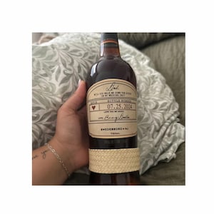 May include: A brown glass bottle with a tan woven label. The label has a handwritten message that reads "Dad, Will you walk me down the aisle on my wedding day?" and "Bottle Number 07.25.2024". The label also includes the text "Love you so much, [Name]"