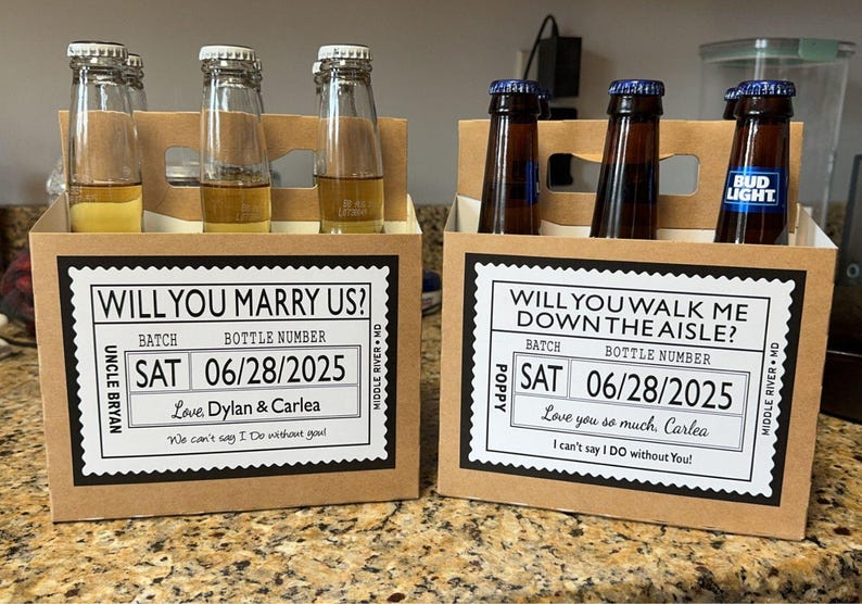 May include: Two cardboard beer carriers with custom labels. One reads "Will You Marry Us?" and the other "Will You Walk Me Down the Aisle?" Each holds beer bottles. The labels include a date, names, and a message.