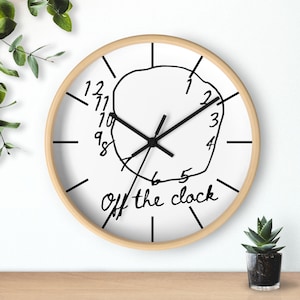 May include: A white round clock with black hands and numbers. The clock face has a black circle with a squiggly line around it. The clock face also has the text "Off the clock" written in black cursive.