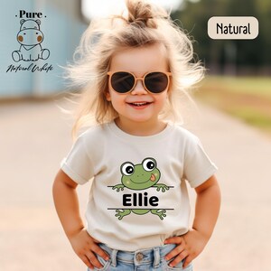 a little girl wearing a t - shirt with a frog on it