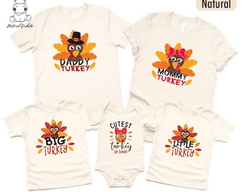 May include: A set of cream-coloured t-shirts and a onesie featuring turkey-themed graphics. The shirts display "Daddy Turkey," "Mommy Turkey," "Big Turkey," and "Little Turkey." The onesie reads "Cutest turkey in town."