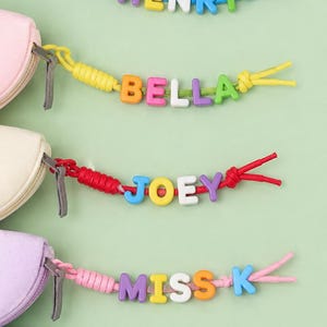 Puede incluir: Cinco estuches pequeños con cremallera en azul claro, rosa, crema, lavanda y verde menta. Cada estuche tiene un tirador de cordón colorido decorado con cuentas de plástico con letras y números que forman HENRY, BELLA, JOEY, MISS K y 2026.