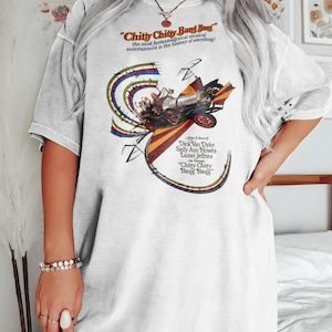 Puede incluir: Camiseta blanca de gran tamaño con un gráfico de estilo vintage de la película "Chitty Chitty Bang Bang". El gráfico presenta una ilustración colorida del coche y el título de la película.