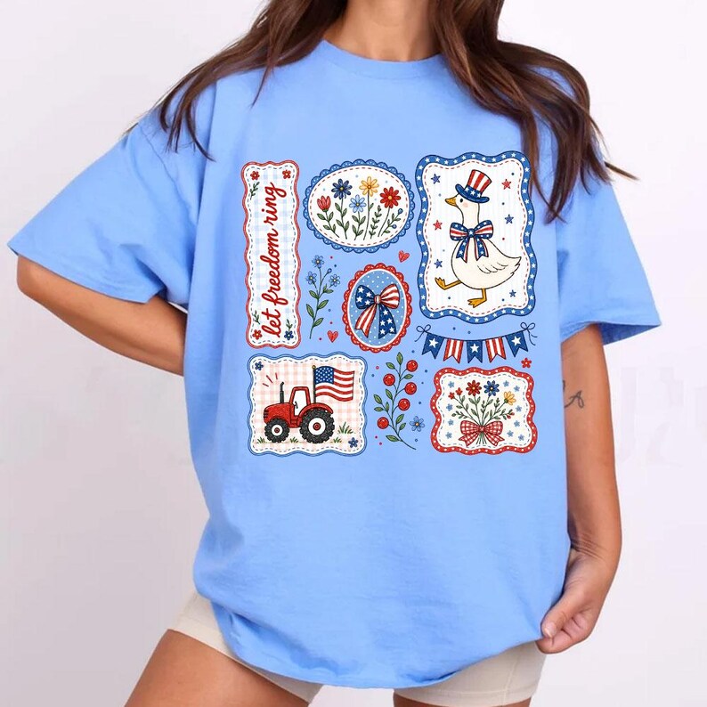 May include: Light blue t-shirt featuring patriotic graphics. Designs include a goose in a top hat, a tractor with an American flag, floral arrangements, and the text "let freedom ring". The graphics are in red, white, and blue.