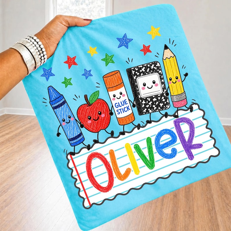 May include: A light blue fabric square featuring a cartoon graphic of a blue crayon, a red apple, an orange glue stick, a black and white composition notebook, and a yellow pencil, with the name Oliver written in colorful letters on lined paper.