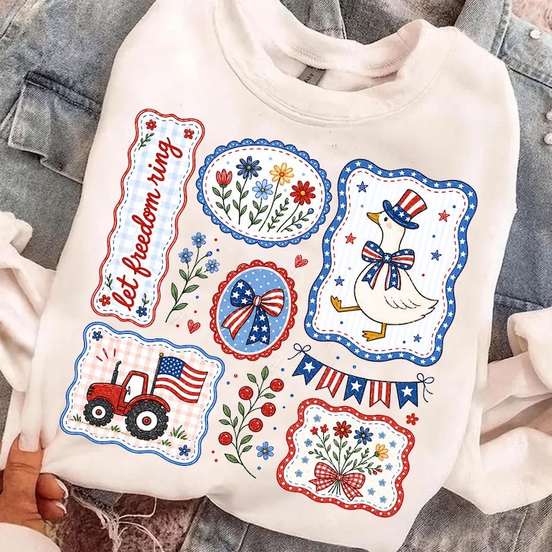 May include: White sweatshirt with patriotic themed graphics. Features a red tractor with an American flag, a goose in a top hat, floral designs, and the text "let freedom ring". The graphics are outlined in red and blue.