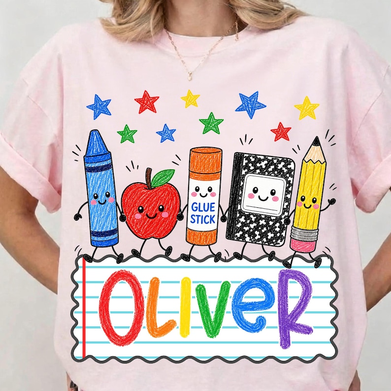 May include: A light pink t-shirt featuring a colorful graphic of a blue crayon, a red apple, an orange glue stick, a black and white composition notebook, and a yellow pencil, all with faces, above the name Oliver written in rainbow letters.