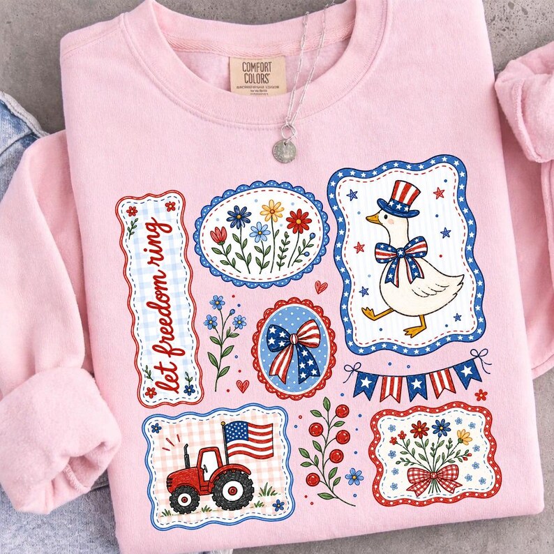 May include: A light pink sweatshirt with patriotic-themed graphics. The design includes a goose wearing a top hat and bow tie, a tractor, floral arrangements, and the text "let freedom ring."