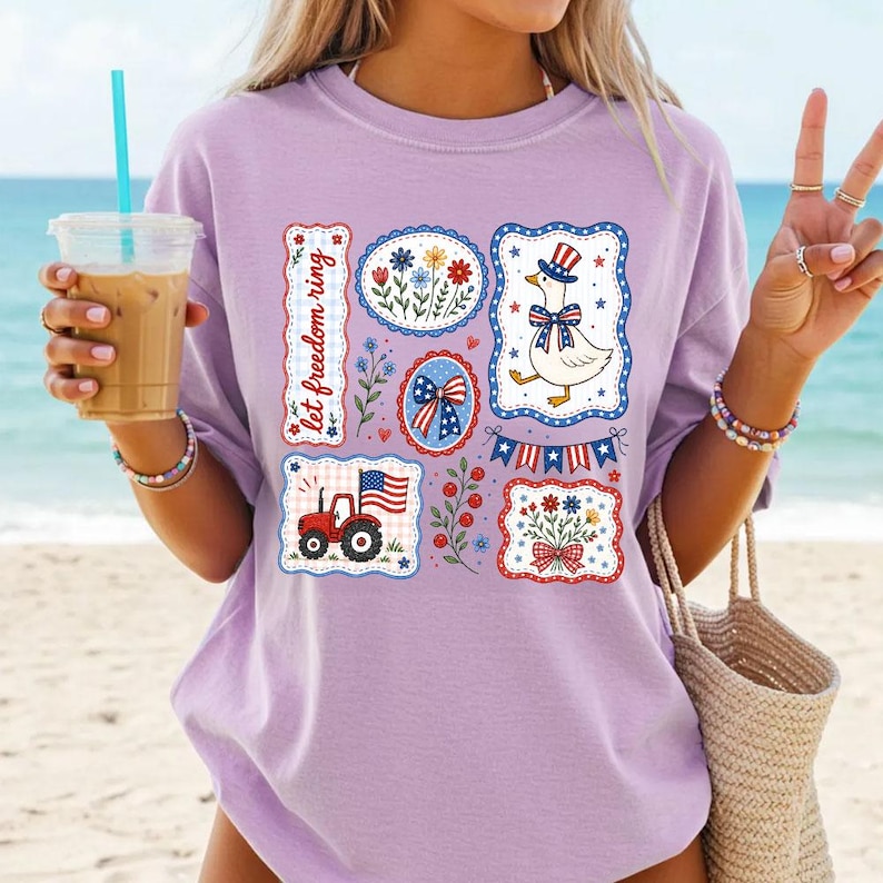 May include: A light purple t-shirt featuring patriotic designs. The shirt displays various patches with floral, flag, and tractor graphics. One patch reads "let freedom ring". The shirt is perfect for celebrating Independence Day.