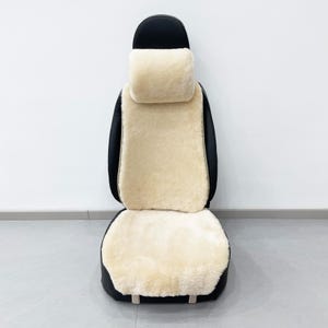 May include: Black car seat cover with a cream-colored sheepskin insert for the seat, back, and headrest. The seat cover has a black border and a cream-colored headrest. The seat cover is designed to fit a car seat.