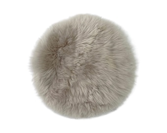 May include: A round, light gray faux fur cushion. The cushion has a soft, fluffy texture and is set against a white background. This decorative pillow adds a touch of comfort and style to any room.