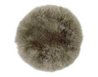 May include: A round, gray sheepskin cushion. The cushion has a fluffy, textured surface and is set against a white background. The cushion is approximately 16 inches in diameter.