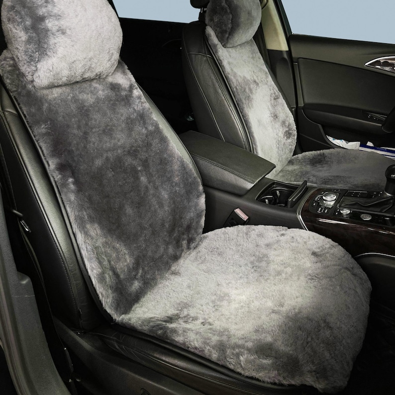 May include: Gray sheepskin car seat covers. The covers are designed to fit over the existing seats, including the headrests. The sheepskin has a soft, plush texture and a medium gray color. The car's interior is black.