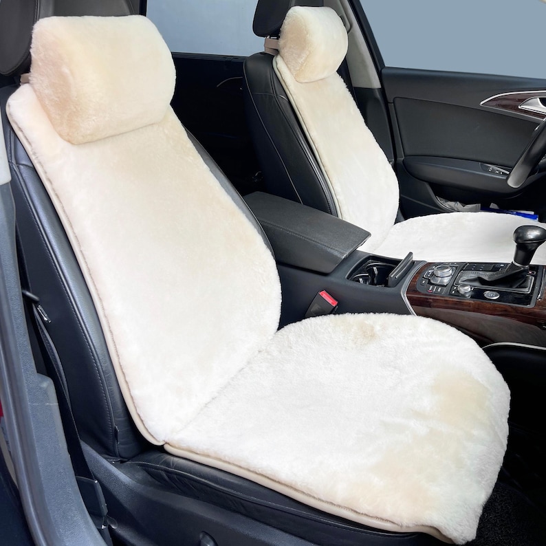 May include: Cream-colored car seat covers with a plush, fuzzy texture. The covers include headrest covers and seat back and bottom sections. The seats are installed in a black leather interior.