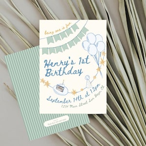 Op de afbeelding: Een verjaardagsuitnodiging met een crèmekleurige achtergrond en blauwe en gouden illustraties. De tekst luidt "Henry's 1st Birthday" met datum en tijd. Een bijpassende envelop met verticale strepen is ook zichtbaar.