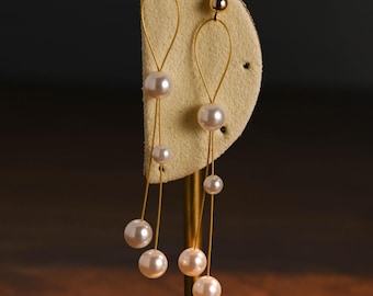 Puede incluir: Elegantes pendientes colgantes dorados con diseño de lágrima. Cada pendiente tiene una pequeña bola dorada en la parte superior y está adornado con múltiples perlas de imitación de varios tamaños. Las perlas cuelgan de delicados hilos dorados.