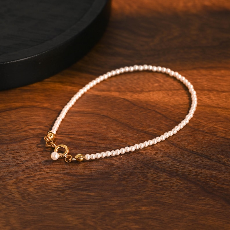 May include: A fine pearl bracelet with a gold clasp, displayed on a dark wood surface. The bracelet is composed of small, round pearls, offering a timeless and refined aesthetic. The gold clasp provides a luxurious accent to the piece.