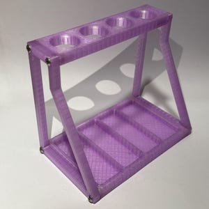 May include: A purple 3D printed stand with four round holes and three rectangular slots. The stand is made of plastic and has a textured surface.
