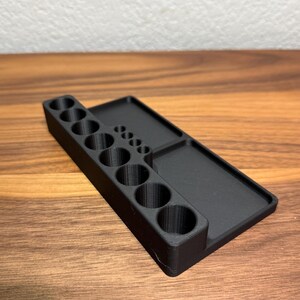 May include: A black plastic organizer with a row of 10 round holes and a flat surface on the right side.