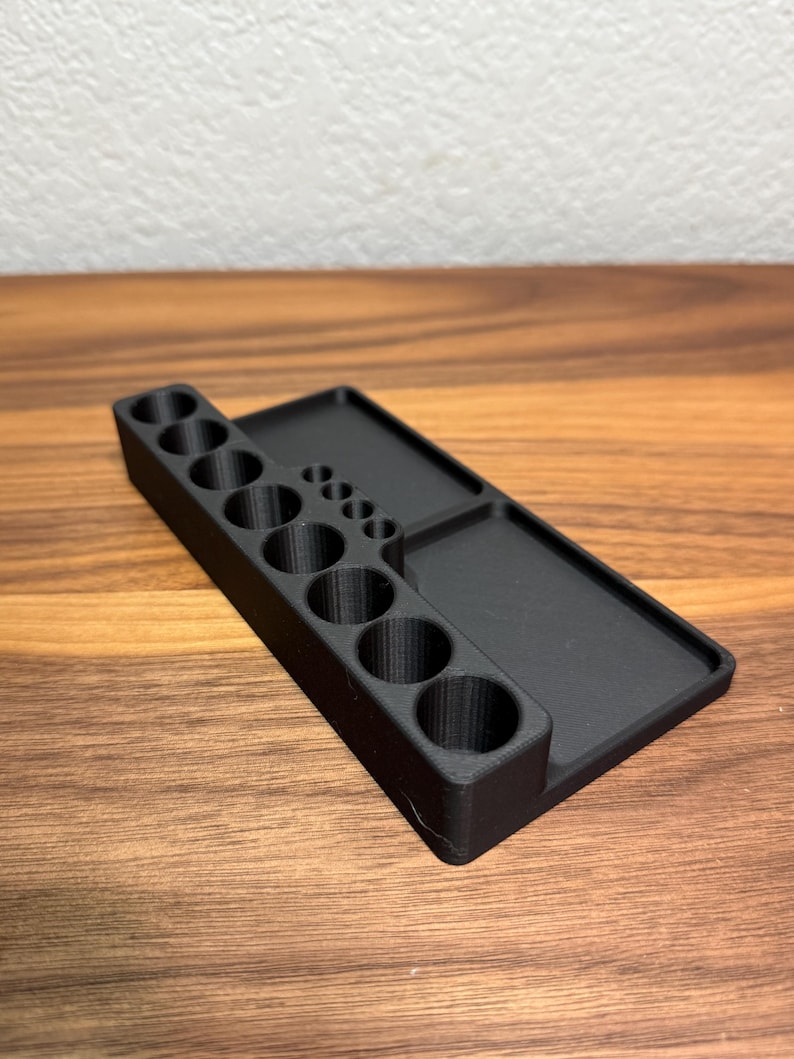 May include: A black plastic organizer with a row of 10 round holes and a flat surface on the right side.